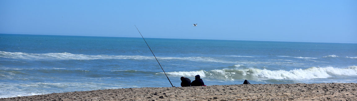 Two Anglers sit hunchedon up against the cold while fishing from the beach along the Skeleton Coast in Namibia.